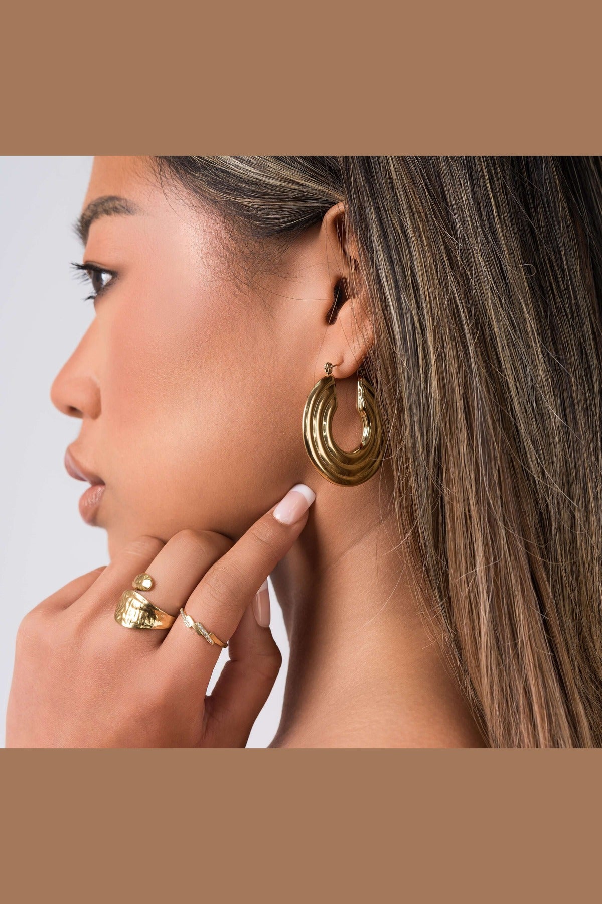 Woman wearing ARIIRA Elia Sculpted Oval Hoop Earrings, showcasing their fluid shape and reflective finish.