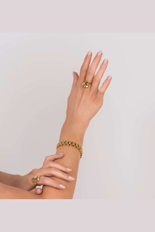 Stylish woman showcasing Raisa Sculpted Link Bracelet with crystal insets and matching gold rings.