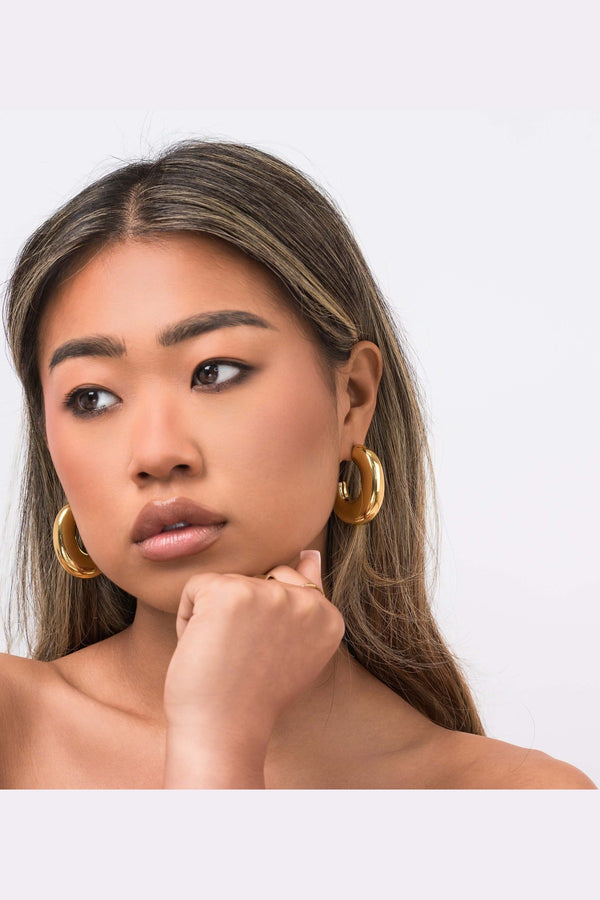 Stylish woman wearing ARIIRA Rhea Sculpted Dome Hoop Earrings, showcasing modern elegance in gold.
