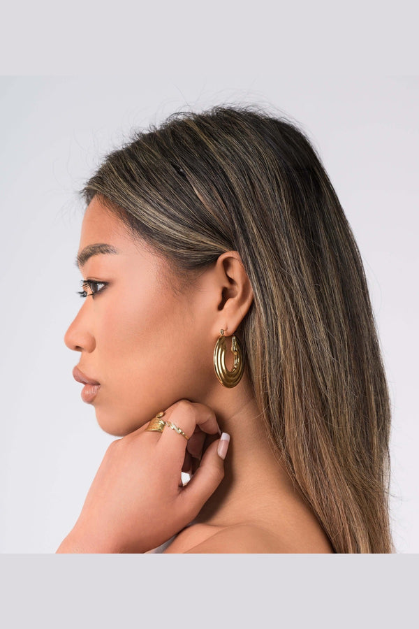 Model wearing Elia Sculpted Oval Hoop Earrings showcasing their reflective finish and lightweight design.