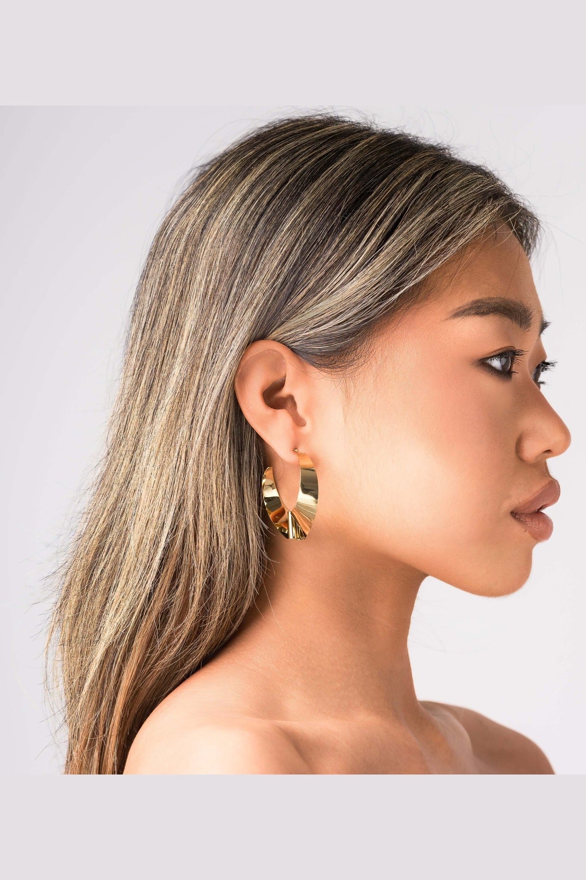 ARIIRA Alma Folded Ribbon Hoop Earrings in gold, showcasing their elegant design on a model's ear.