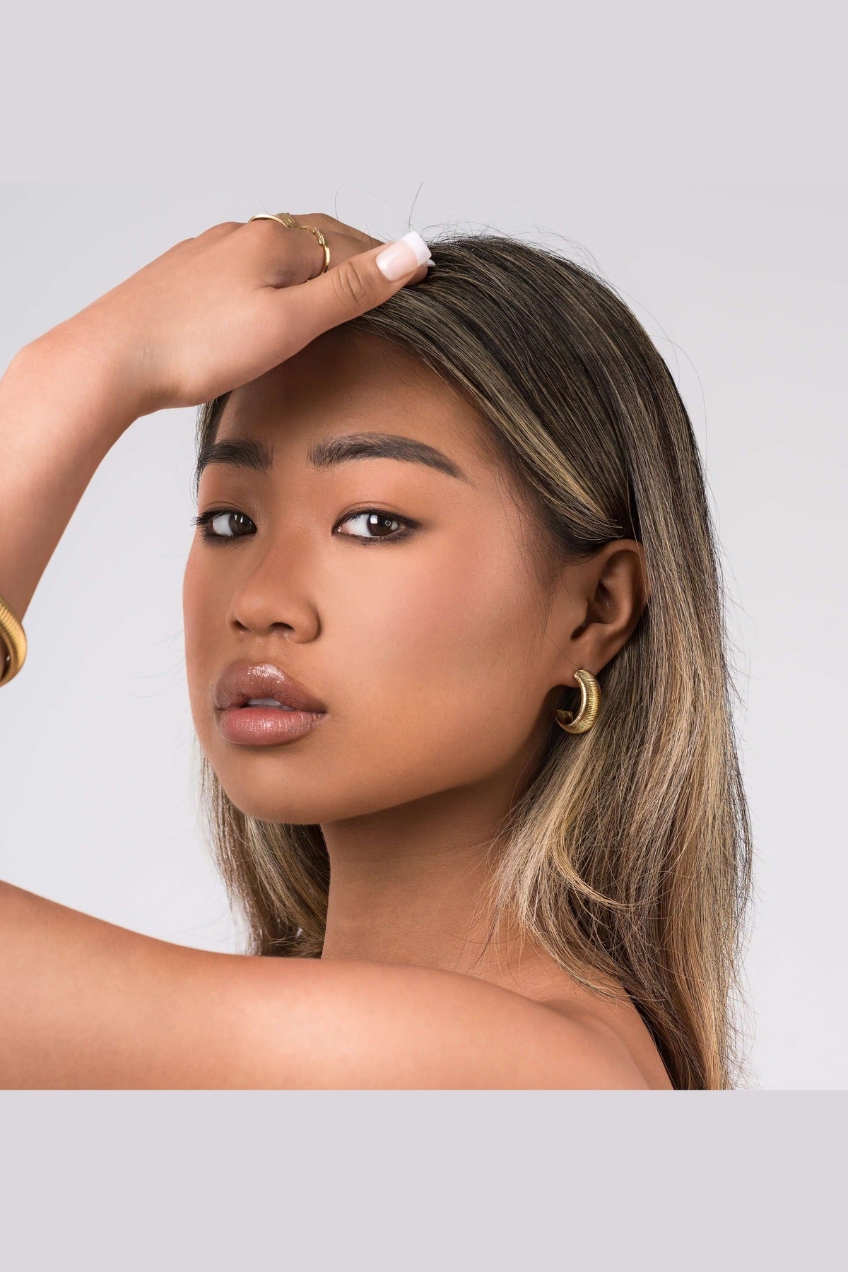 Young woman showcasing Selene Ribbed Hoop Earrings, featuring fine ridged detailing and a polished brushed finish.