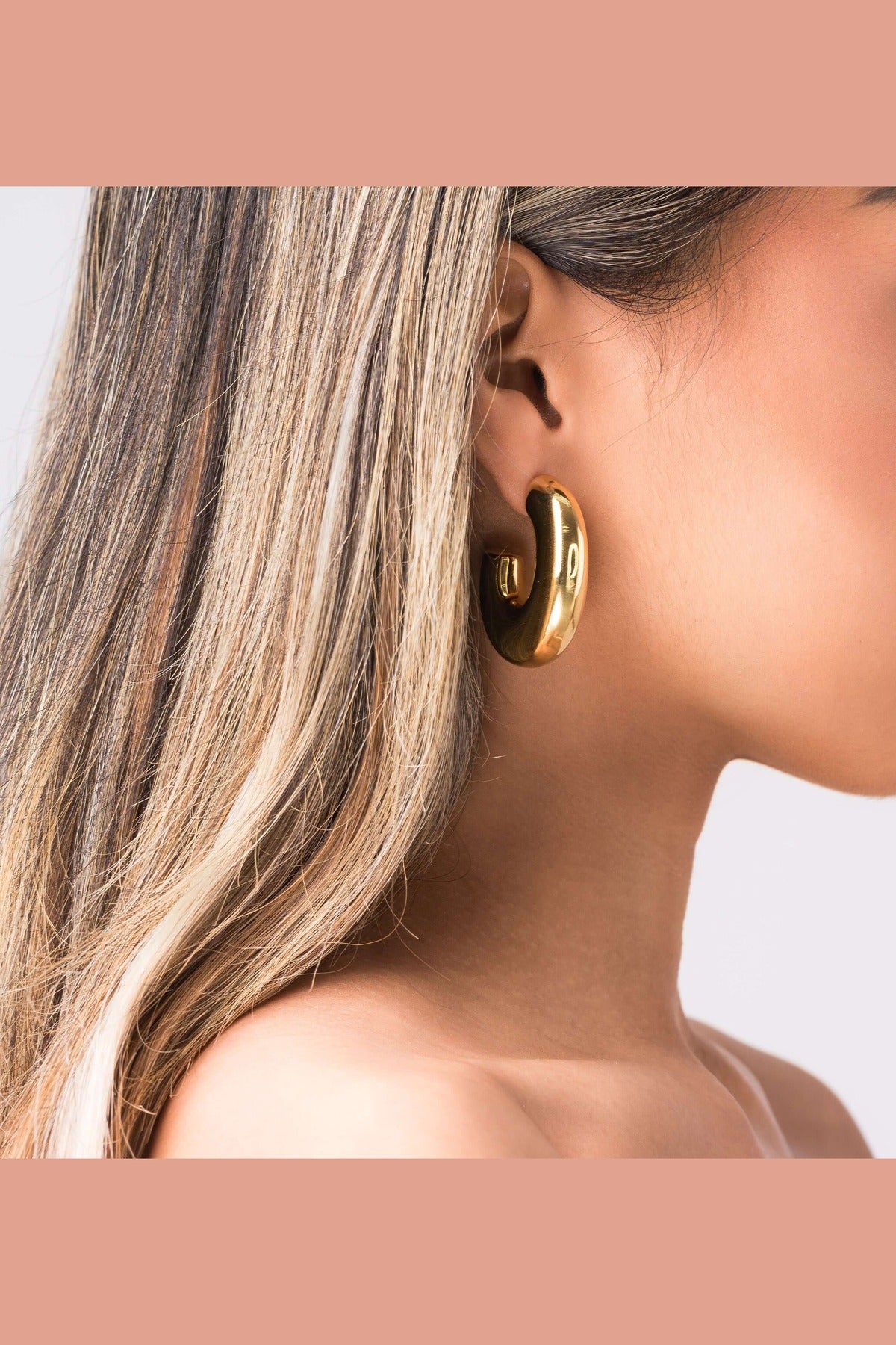 Close-up of a model wearing ARIIRA Rhea Sculpted Dome Hoop Earrings in polished gold.