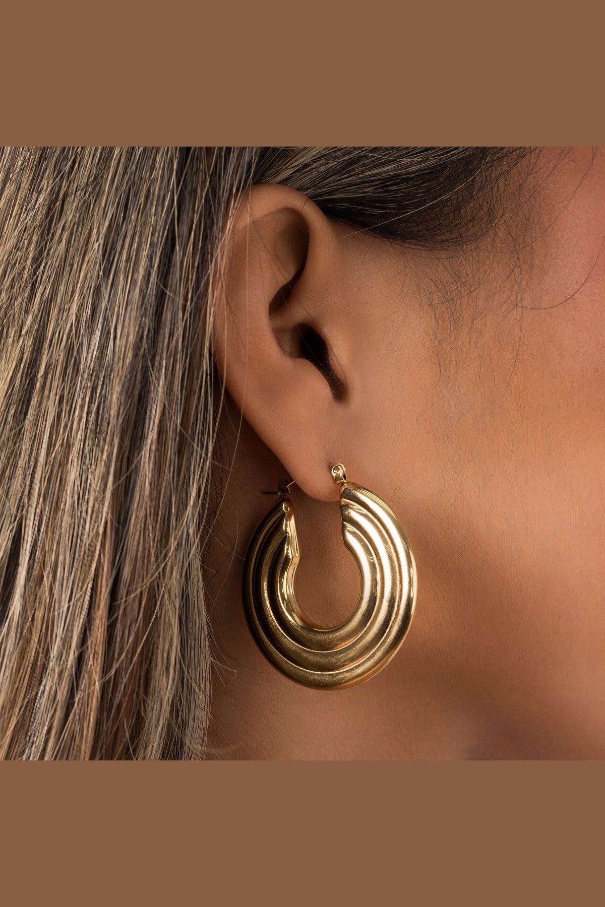 Stylish Elia Sculpted Oval Hoop Earrings in gold featuring ridged design, showcasing a close-up on an ear.